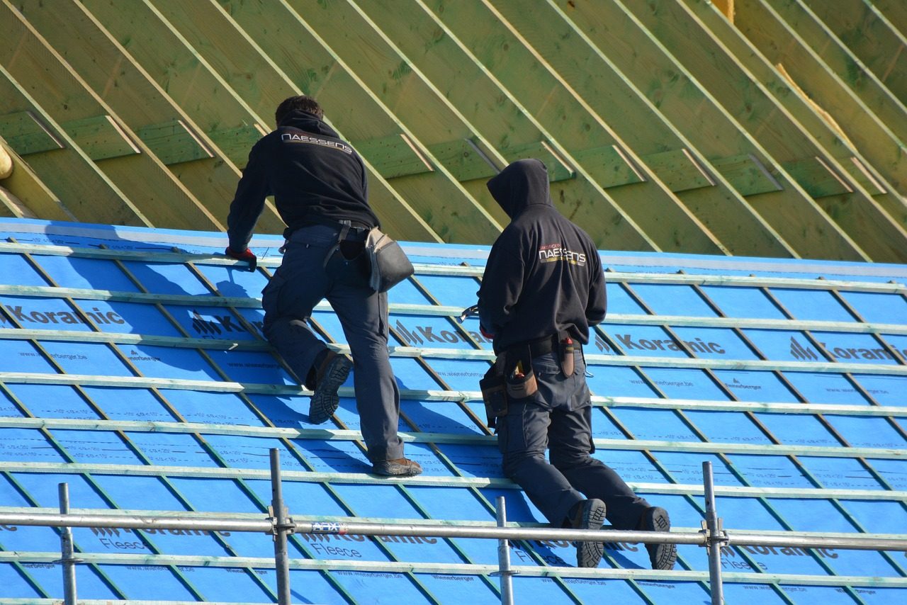 Two roofers working on blue underlayment on a pitched roof