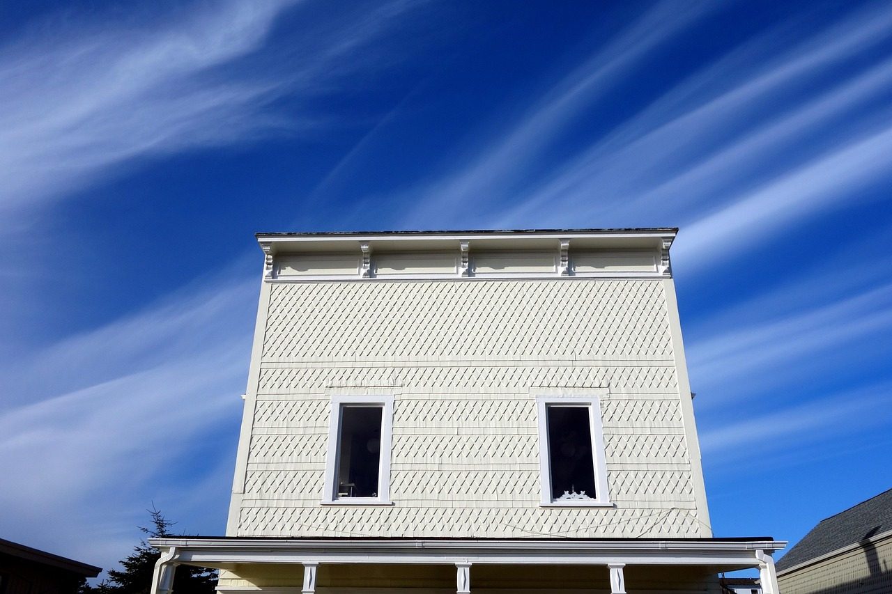 Two-storey house with cream shingles and white trim under a blue sky
